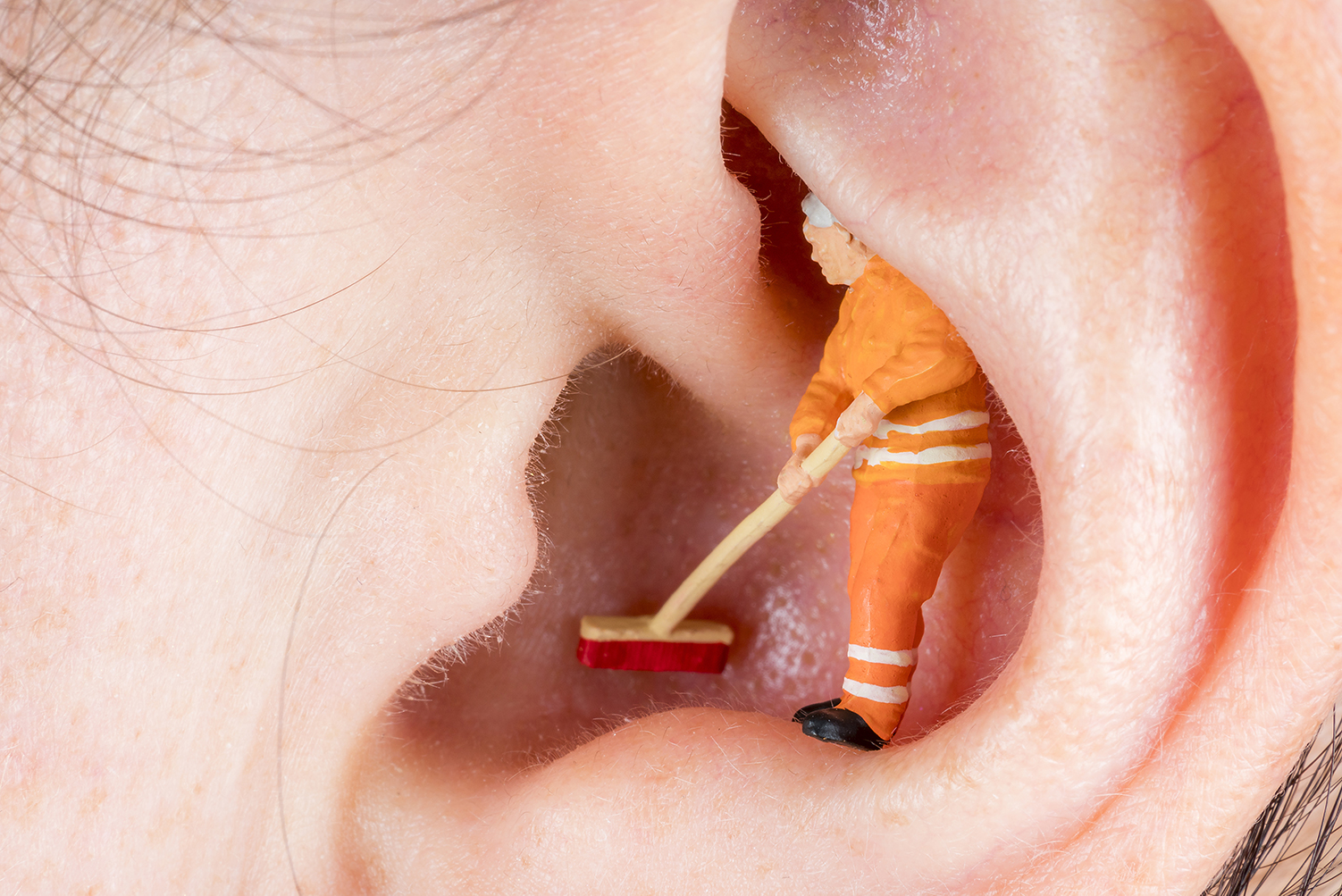 Überdimensionierte Darstellung eines Ohres in dem ein Mann steht und es ausfegt.