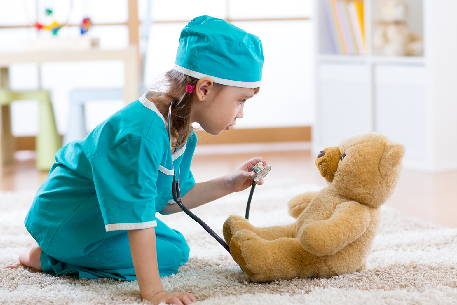 Kind im Arztkittel untersucht einen Teddy mit einem Stethoskop.