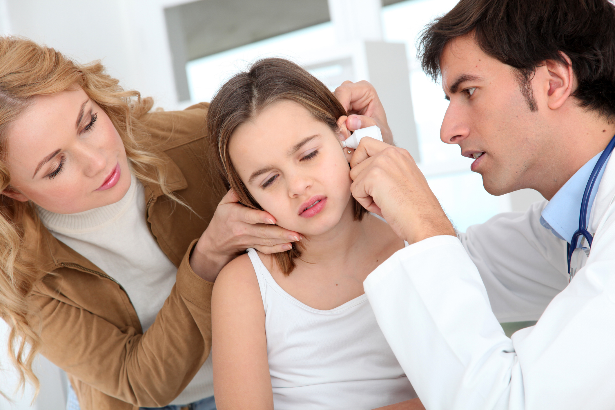 Arzt untersucht das Ohr eines Mädchens, während ihre Mutter sie tröstet.