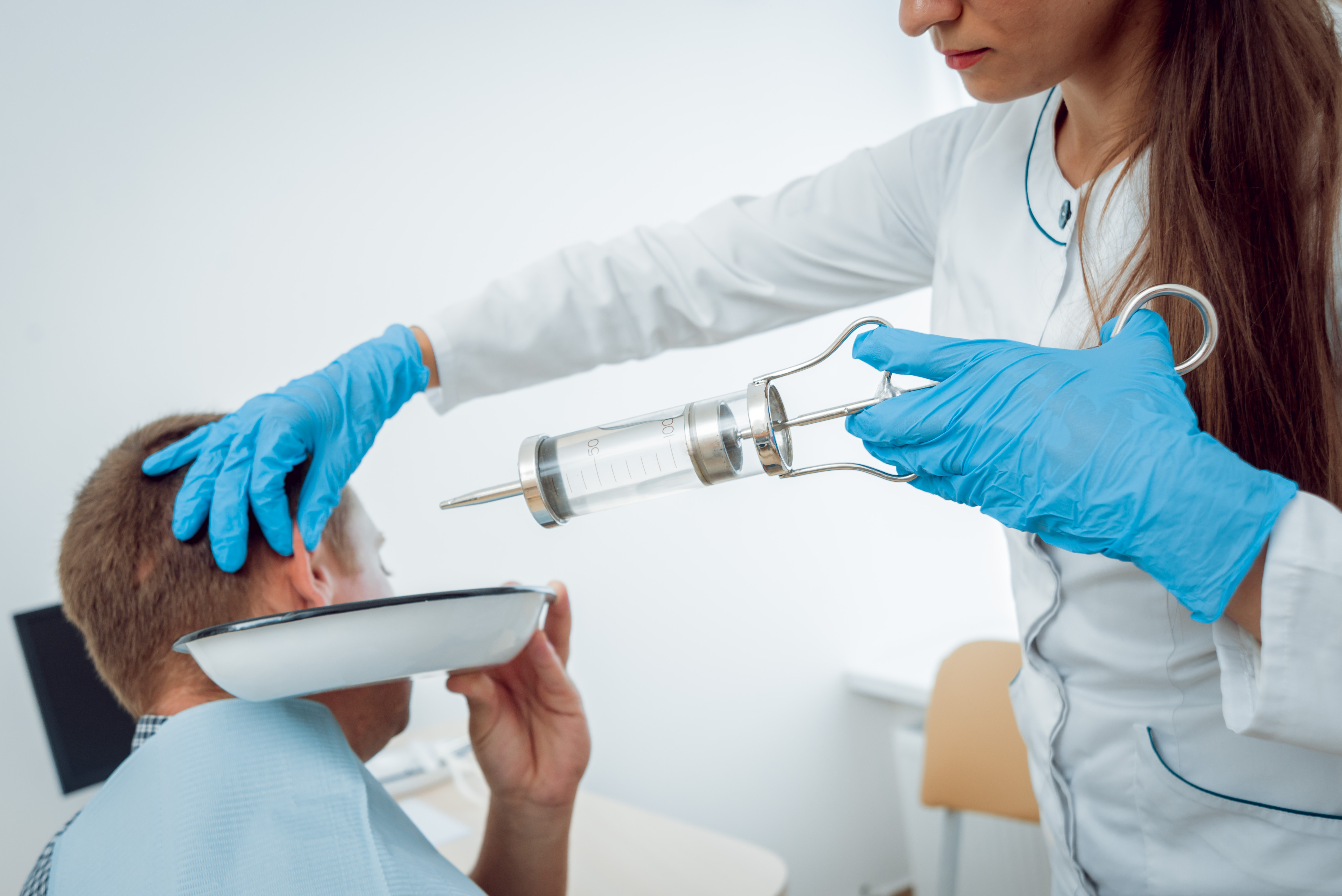 Ärztin hält eine Spritze für eine Ohrenspülung an das Ohr eines Patienten.